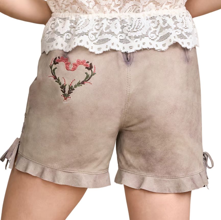 Back view of women’s traditional beige lederhosen shorts featuring embroidered pink floral heart design and ruffled hems, paired with a lace blouse.